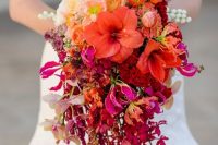a super bright cascading wedding bouquet of blush, orange, red, burgundy and purple blooms and branches hanging