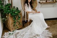 an embellished lace wedding dress with a plunging neckline, short sleeves with fringe and long fringe on the edge of the dress