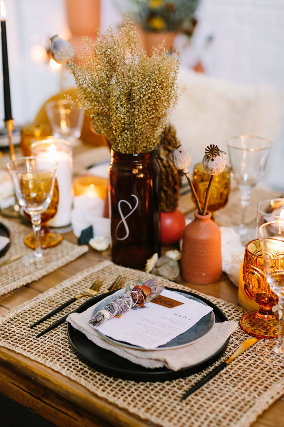 The wedding tablescape was done with woven placemats, dried blooms and foliage, elegant cutlery, amber glasses and terracotta vases