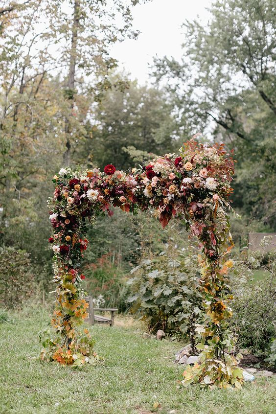a super lush floral wedding arch in burgundy and pink shades, with lots of fall leaves to embrace the season and with an ombre effect
