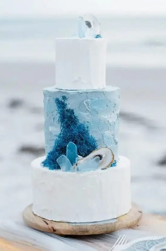 a beach-inspired wedding cake with blue and white textural tiers, with sugar corals, seaglass and seashells is amazing