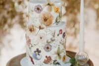 a beautiful white buttercream wedding cake with white, lilac, yellow pressed flowers and greenery looks incredibly chic