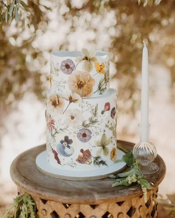 a beautiful white buttercream wedding cake with white, lilac, yellow pressed flowers and greenery looks incredibly chic