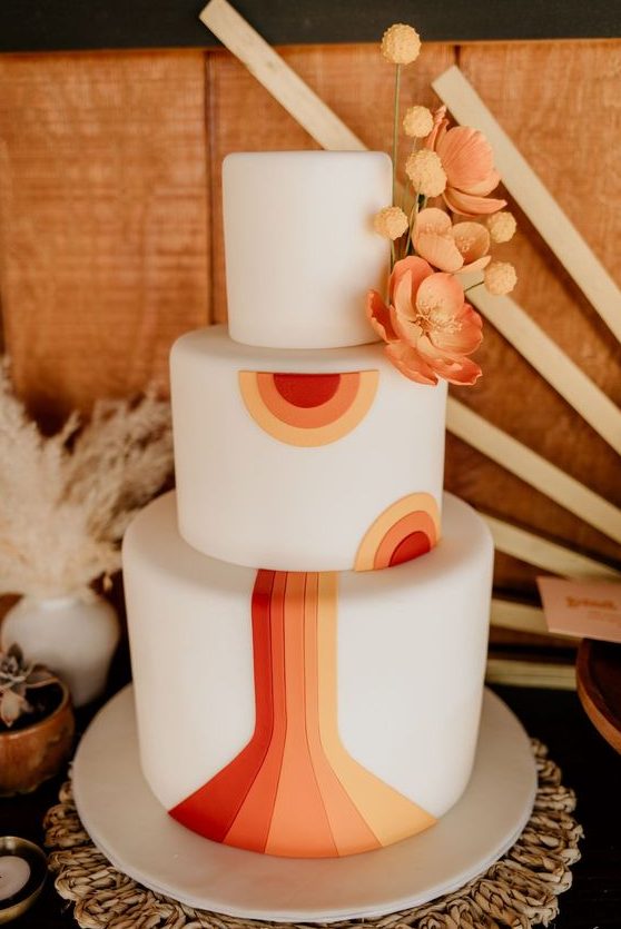 a bold and chic 70s wedding cake in white, with red, orange and yellow detailing and orange sugar blooms and billy balls