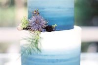 a bright ombre blue wedding cake from white to light blue and navy, succulents, greenery, berries and thistles for a seaside wedding
