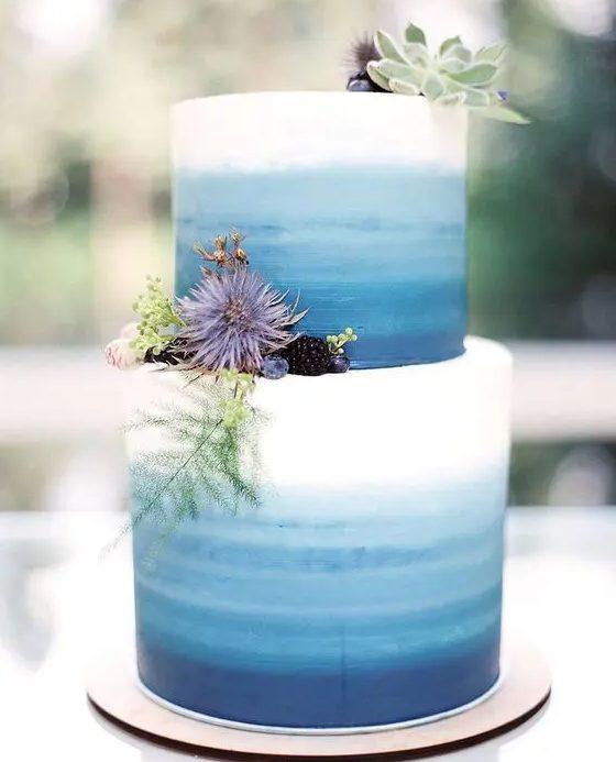 a bright ombre blue wedding cake from white to light blue and navy, succulents, greenery, berries and thistles for a seaside wedding
