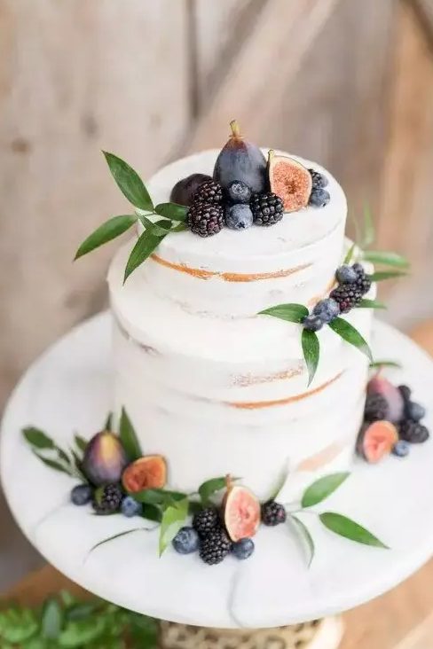 A delicate and pretty fall vineyard wedding cake   a semi naked piece topped with fresh greenery, figs, blackberries and blueberries