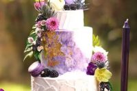 a dreamy and whimsical wedding cake with textural buttercream and a watercolor purple tier, with gold leaf, purple macarons, berries and bright blooms for a fairytale wedding