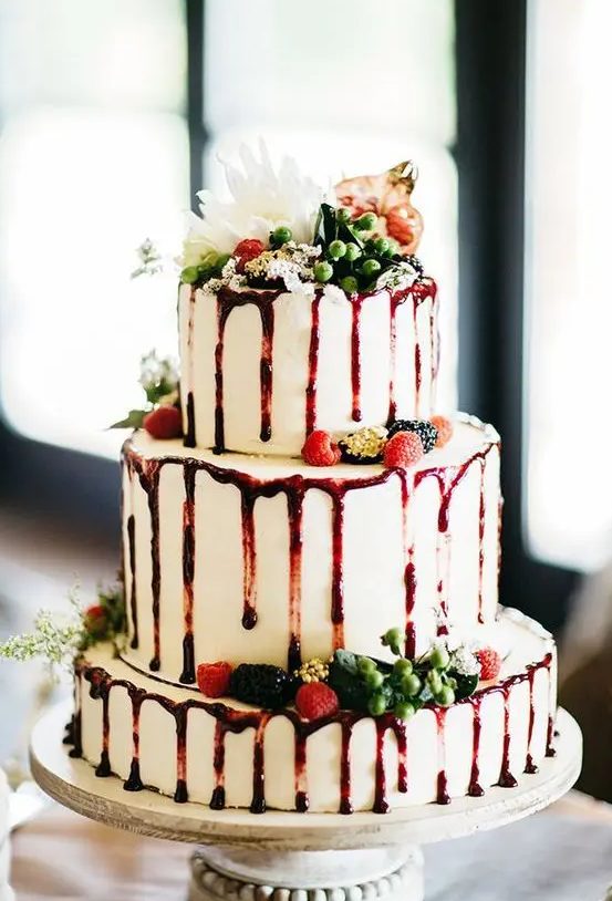 a fantastic Christmas drip wedding cake with berry sauce, fresh berries, greenery and a white bloom on top is wow