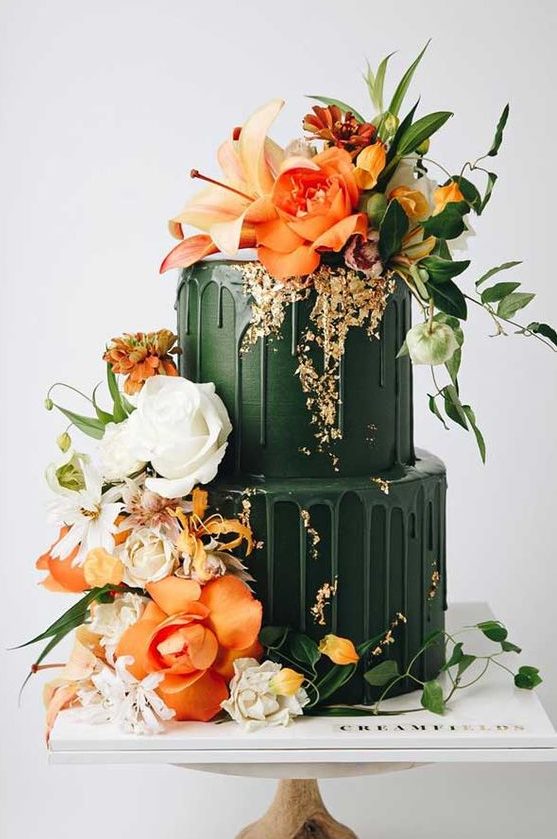 A gorgeous dark green wedding cake with matchign drip and bold orange and white blooms and greenery looks jaw dropping