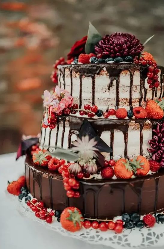 a gorgeous naked wedding cake with chocolate drip, fresh berries and blooms is a fantastic idea for a boho or rustic wedding in the fall