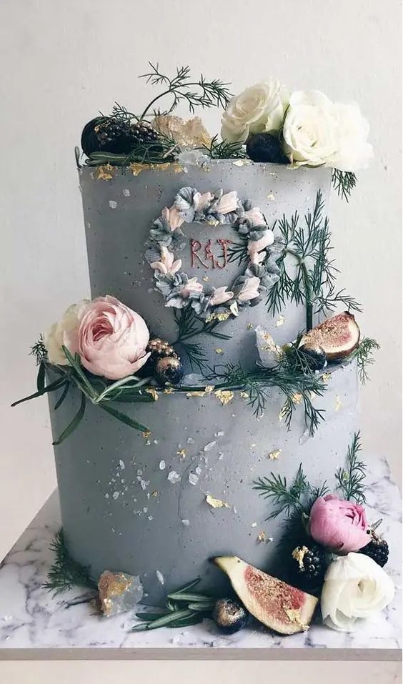 a grey textural wedding cake with fresh blooms, greenery, crystals, gold leaf and fruits plus a copper monogram