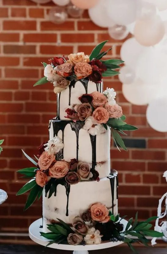a jaw dropping three tier wedding cake with chocolate drip, mauve and peachy blooms, greenery is a chic idea for any wedding