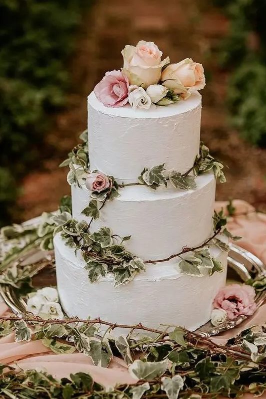 a lovely white buttercream wedding cake decorated with greenery, pink and blush roses is a pretty idea for a secret garden wedding