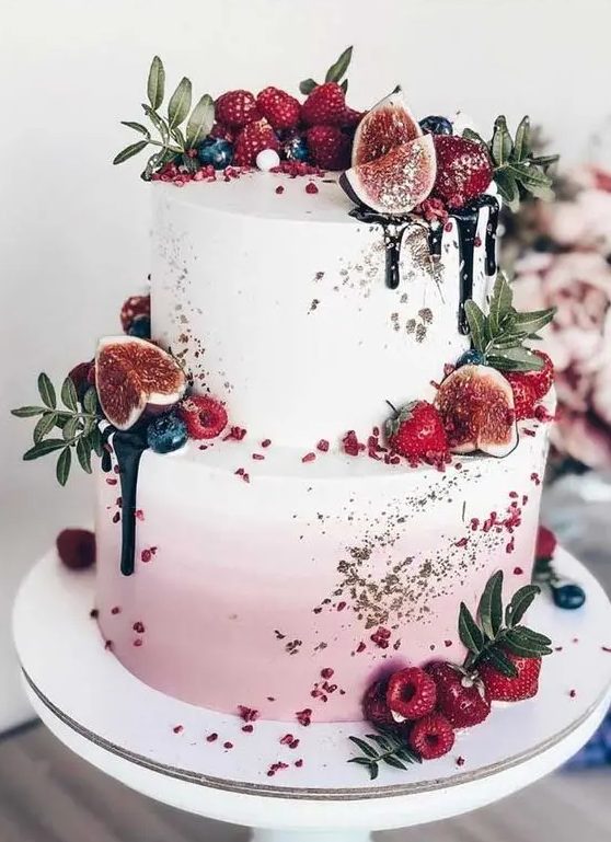 A mouth watering ombre pink wedding cake with gold glitter, chocolate drip, fresh fruit, berries and greenery is amazing for summer