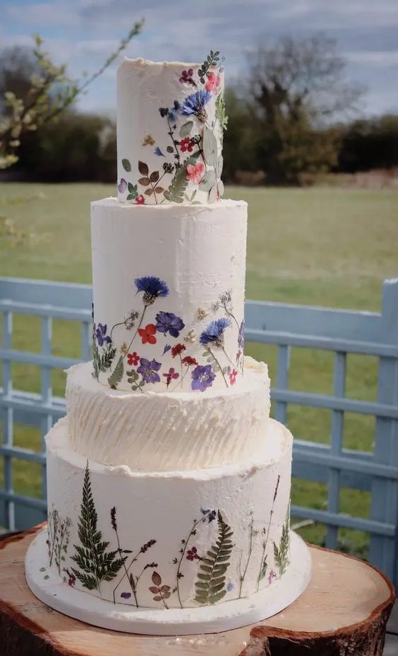 a multi-tier white buttercream wedding cake with bold pressed flowers and leaves is a fabulous idea for a bright summer wedding