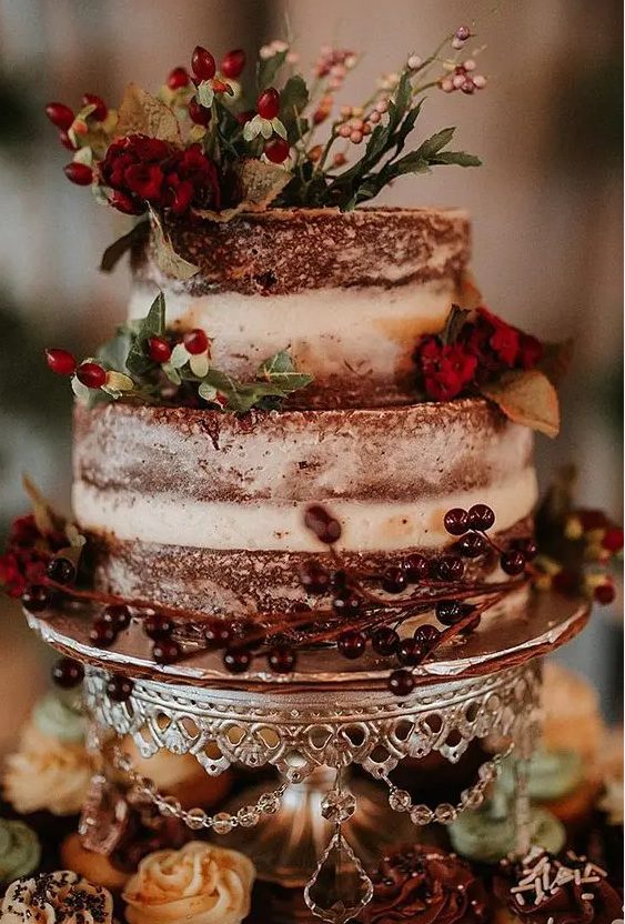 a naked chocolate wedding cake with berries, red blooms and greenery for a rustic winter wedding