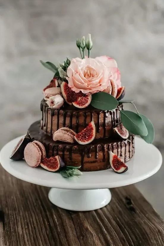 A naked chocolate wedding cake with chocolate drip, pink macarons, blooms, greenery and fresh figs is a delicious looking and lovely idea for a wedding