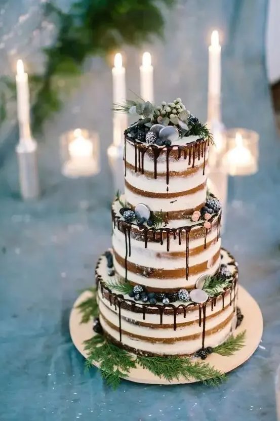 a naked wedding cake with chocolate drip, sugared berries, greenery and ferns is a stylish option for a winter wedding