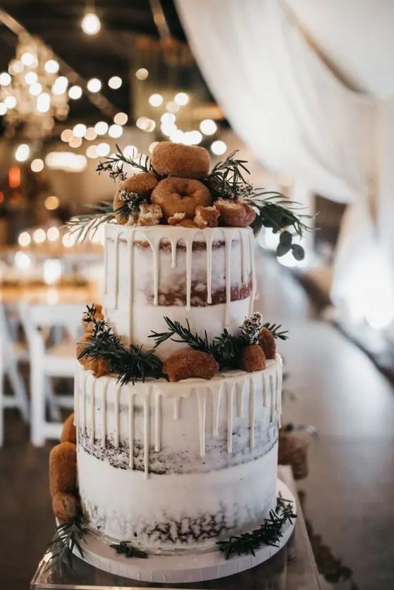a naked wedding cake with creamy drip, topped with evergreens and donuts is a cool idea for a winter wedding