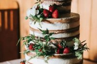 a naked wedding cake with fresh strawberries, greenery and white blooms plus a topper for a summer rustic wedding