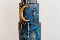 a navy galaxy-themed wedding cake with gold arrows and rays, with a half moon is perfect for a celestial wedding