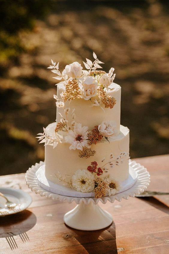 a neutral wedding cake with blush and neutral blooms and white dried leaves is a cool idea for a summer boho wedding