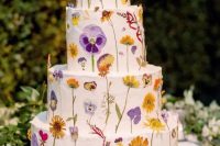a pretty multi-tier white buttercream wedding cake with bright pressed flowers and leaves is a fun and cool idea for spring and summer weddings