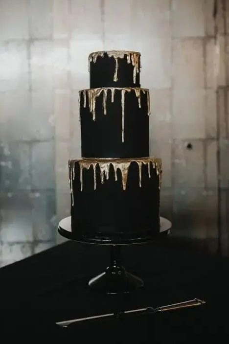 a refined and contrasting matte black wedding cake with gold dripping is a stylish modern idea, suitable for a Halloween or NYE wedding, too