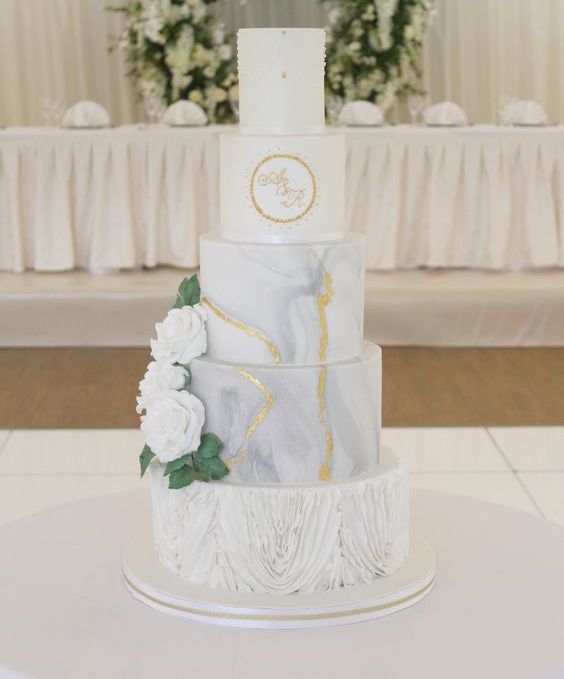 a refined five tier wedding cake with ruffle, marble and textural tiers, with gold touches and sugar blooms