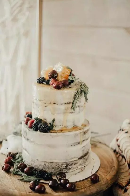 a semi-naked wedding cake with caramel drip, fresh berries and fruit and greenery is a gorgeous boho wedding dessert for a vineyard wedding