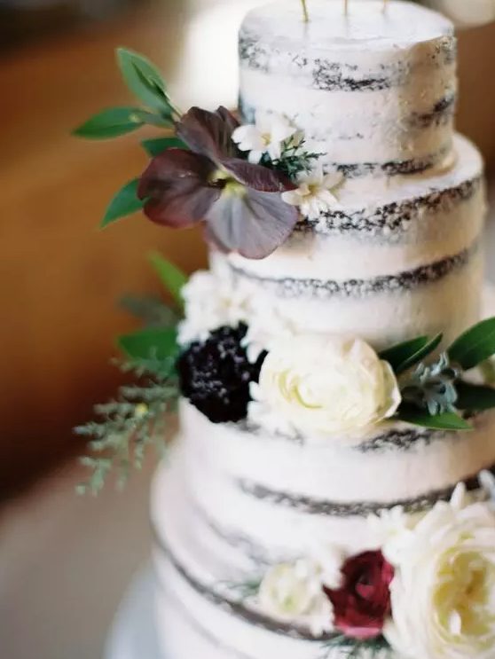 A semi naked wedding cake with white and burgundy blooms, greenery is a lovely idea for a fall vineyard wedding