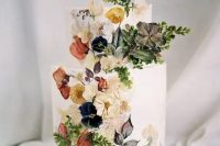 a sophisticated white buttercream wedding cake with pressed dried flowers and some fresh blooms and leaves attached to the cake