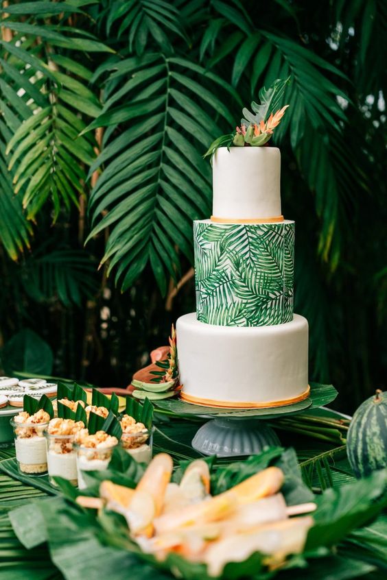 a tropical three tier wedding cake with white and tropical print tiers and tropical leaves on top is a bold and cool idea