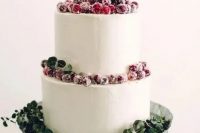 a white buttercream wedding cake decorated with greenery and sugared berries is a stylish idea