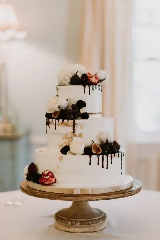 a white wedding cake with chocolate drip, cotton, figs and berries and white blooms on top is wow