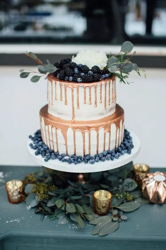 an elegant winter wedding cake with copper drip, fresh berries, greenery and a white bloom on top is a cool and catchy idea