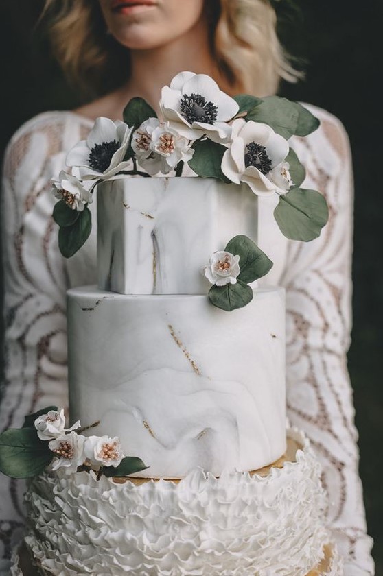 a beautiful wedding cake with marble and ruffle tiers and gold leaf and blooms and leaves on top for a refined wedding