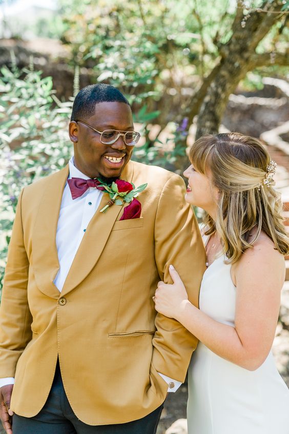 a bold groom's look with a mustard blazer, black pants, a white shirt, a burgundy bow tie and a bold handkerchief
