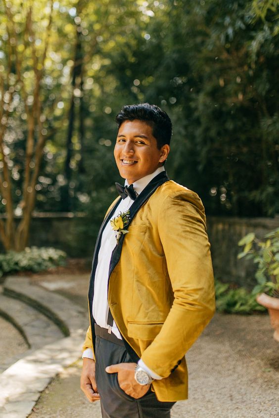 a catchy and refined groom's outfit with a mustard tuxedo with black lapels, a black bow tie, a white shirt and black trousers