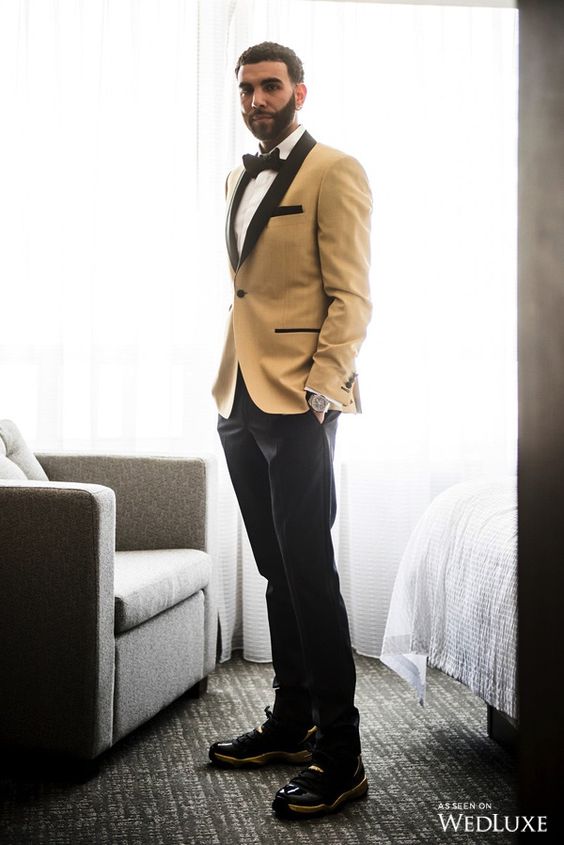 a catchy groom's look with a white shirt, a mustard tuxedo with black lapels, a black bow tie, black trousers and shoes