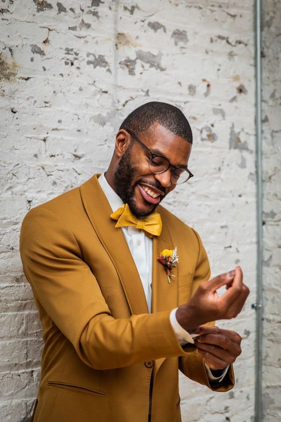 a chic mustard groom's look with a suit, a white shirt, a yellow bow tie, a bold boutonniere is a lovely idea