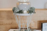 a grey and white wedding cake with gold foil and some greenery for a glam modern wedding