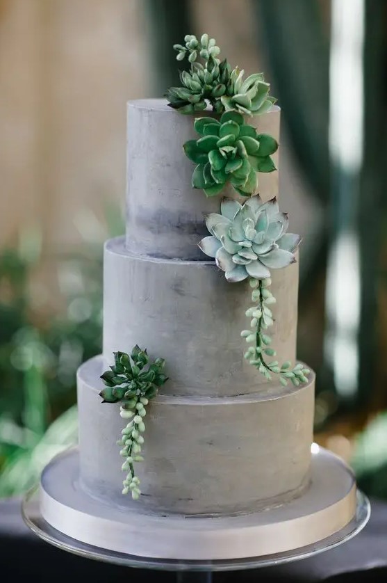 A grey concrete like wedding cake with plain tiers and succulents for decor is a very chic and modern dessert
