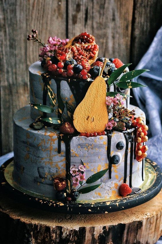 a grey concrete wedding cake topped with chocolate drip, fresh berries, bright blooms, a pear slice and greenery is wow