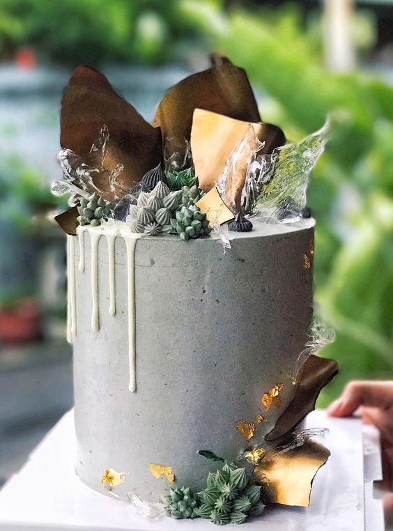 a grey concrete wedding cake with creamy drip, fresh berries, meringues, chocolate bark and some clear splashes on top for a modern wedding