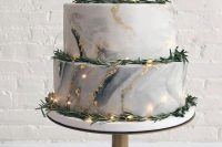 a grey marble wedding cake with gold glitter and foil, greenery, a calligraphy topper and some lights for a modern wedding