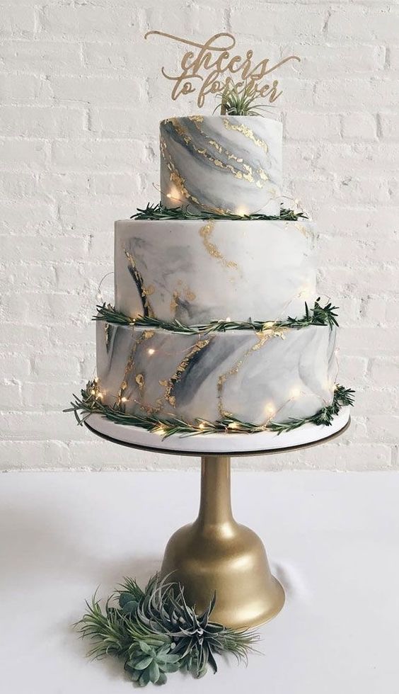 a grey marble wedding cake with gold glitter and foil, greenery, a calligraphy topper and some lights for a modern wedding