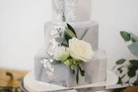 a grey marble wedding cake with mismatching tiers, silver foil and a white bloom for a spring or summer wedding