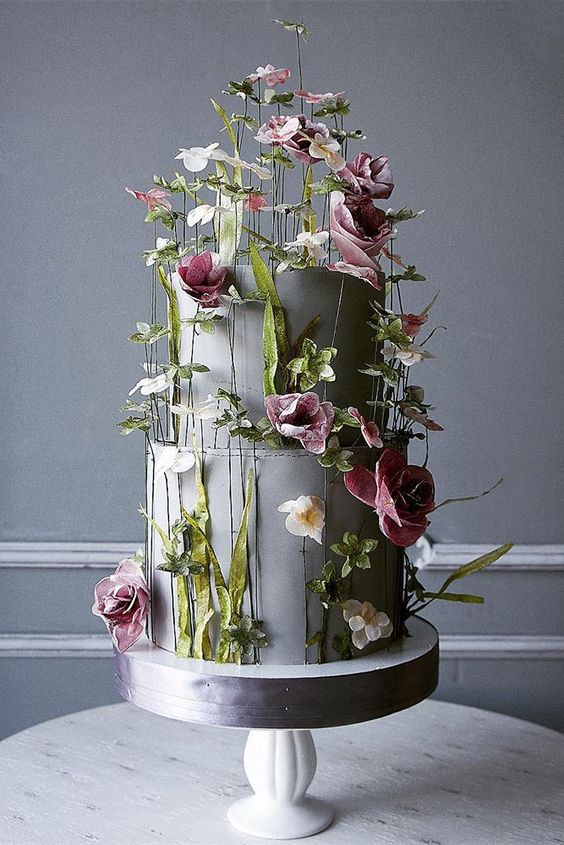 a grey plain wedding cake all dotted with real greenery and pink and white blooms is very refined and artistic